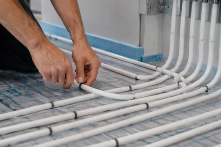 Underfloor heating installation, hands attach the white heating pipe to the insulation board, underfloor heating installers are familiar with both wet and dry installation systems.