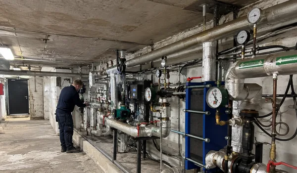 Maintenance and repair of the heating substation, plumber in the basement heating substation by the pipeline, blue plate heat exchanger and pressure gauges in the foreground, 153 heating units were maintained and repaired in 2025.
