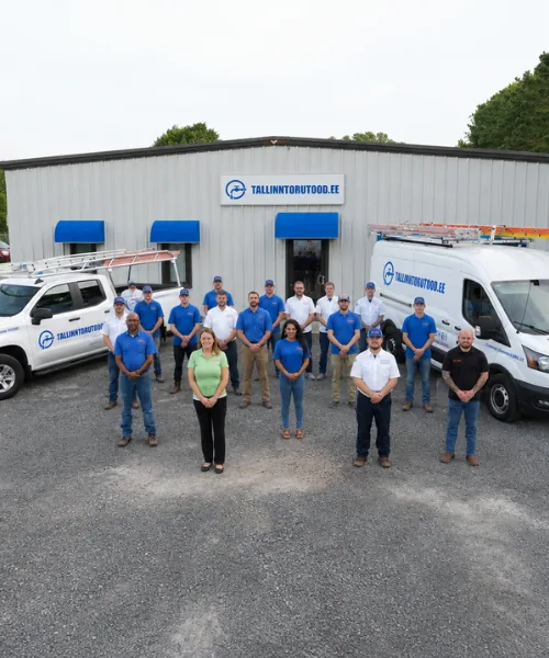 People stand in rows in front of a gray warehouse with the sign TALLINNTORUTOOD.EE between a white pick-up truck and a van with a ladder, a copy of the shut-off valve diagram of each contracted house is kept in the warehouse so that the on-duty foreman can find the right valve in case of an evening emergency.