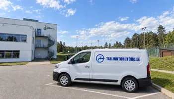 A white van with a water faucet with a circular logo and the words TALLINNTORUTOOD.EE under the pine trees next to the white balcony house of the Keila Music School, when changing the section of the cast-iron riser, the plumber fastens the upper cast-iron pipe to the wall with a clamp before cutting.