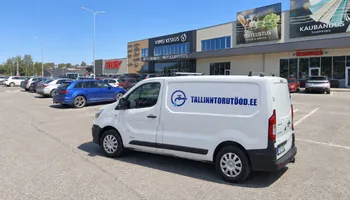 A white van with a water faucet with a circular logo and the inscription TALLINNTORUTOOD.EE in front of the commercial building of Viimsi Keskus next to other cars in the sunshine, during an emergency call, the plumber instructs the caller on turning off the water.
