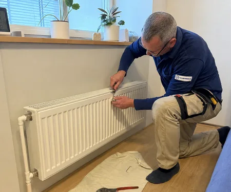 A plumber works at the top edge of a panel radiator on the wall, radiator fitters know the threads and connections of both Soviet-era and modern radiator valves.