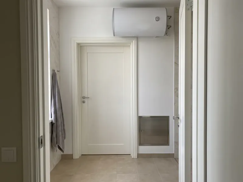Mustamäe korteri vannitoa eesruum ukseavast: WC ukse kohal valge horisontaalne boiler, seina all jaotuskapi metalluuk ja nagis hall rätik, jaotuskapi luuk avaneb käsitsi ilma kruvikeerajata, et klient jõuaks sulgeventiilini kohe.