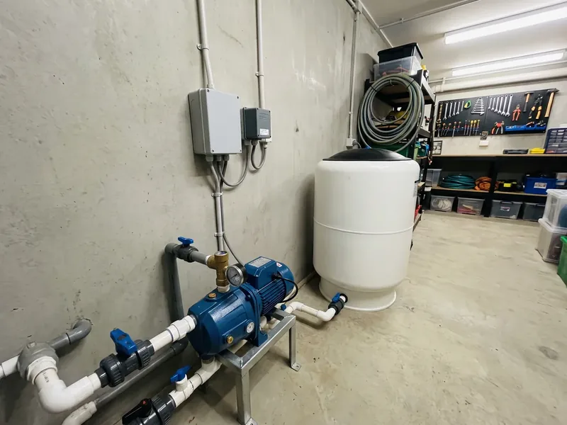 Saue valla eramu tehnoruumis sinine pump metalljalal, valge membraanpaak, plasttorude sinised kraanid ja seinal kaks halli elektrikarpi, puurkaevu imitoru otsas on jalgklapp, mis hoiab imitoru pumba seiskudes veega täis.