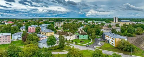 Drone image of Maardu: a curving street leads between pastel two-story residential buildings and dense foliage to a single high-rise building standing on the horizon, 63 connection routes will have been built to the detached houses of Vana-Maardu and Uusküla by the end of 2025.