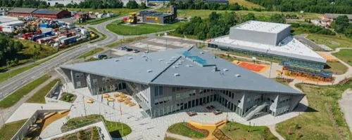 Drone image of Rae municipality: a sports hall with a white roof, a stadium and a yard of a large building with wooden benches, in the townhouses of Peetri and Järveküla, 438 underfloor heating actuators have been replaced by the end of 2025.
